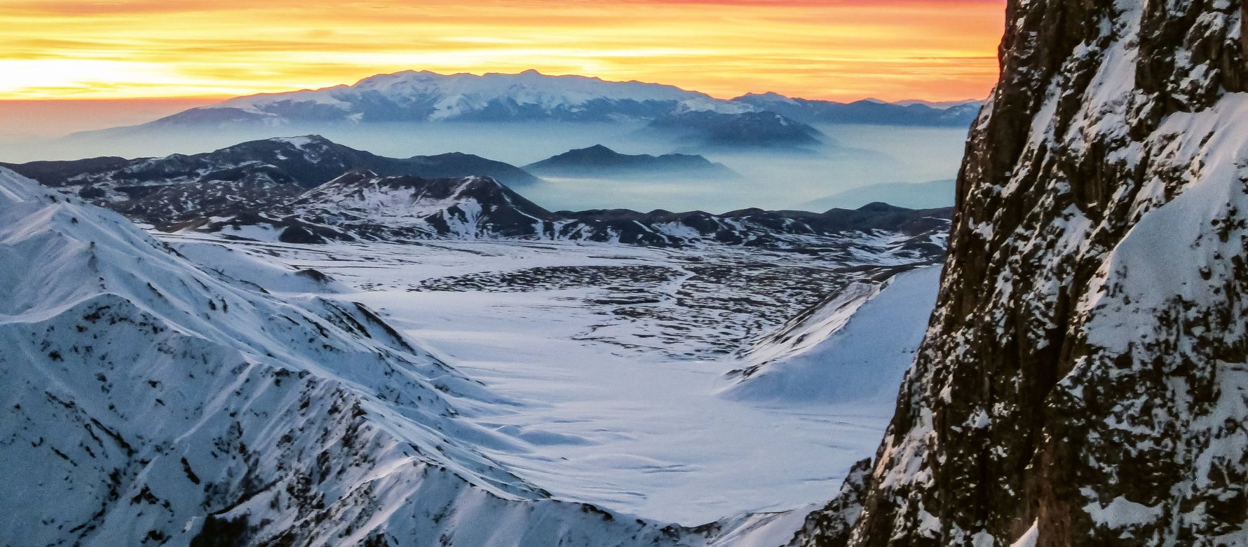 Fotografia invernale di un'alba tra monti con al centro un'altopiano innevato