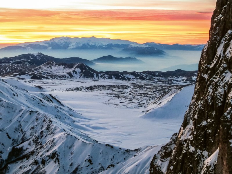 Fotografia invernale di un'alba tra monti con al centro un'altopiano innevato